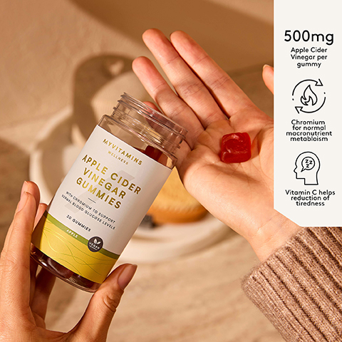 Hand holds a bottle of Myvitamins Apple Cider Vinegar Gummies and a single gummy, with text overlay 500mg Apple Cider Vinegar per gummy, Chromium for normal macronutrient metabolism, Vitamin C helps reduction of tiredness, and text on the bottle label MYVITAMINS WELLNESS APPLE CIDER VINEGAR GUMMIES WITH CHROMIUM TO SUPPORT NORMAL BLOOD GLUCOSE LEVELS 30 GUMMIES APPLE VEGAN FRIENDLY.