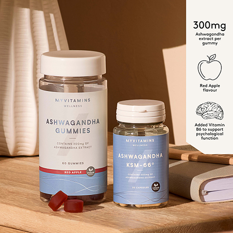 Two Myvitamins Ashwagandha supplements are shown on a wooden surface: a clear bottle of 60 red Ashwagandha Gummies in Red Apple flavour, containing 300mg Ashwagandha extract per gummy and with added Vitamin B6 for psychological function, and a blue bottle of 30 Ashwagandha KSM-66® capsules containing 500mg Ashwagandha extract, both products marked Vegan Friendly.